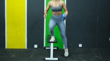 Gri eşofmanlı güzel bayan sporcu spor salonunda bacak egzersizi yapıyor.
