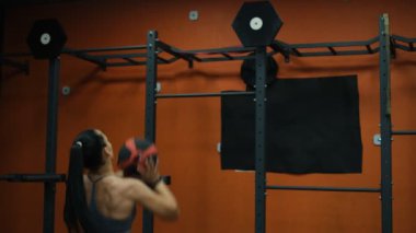 Güzel kaslı sporcu kadın, jimnastik topunun arkasında dururken topu fırlatıyor.