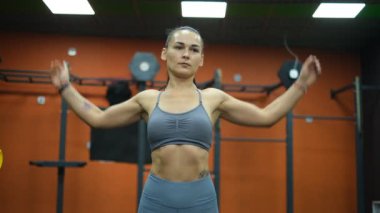 Gri takım elbiseli güzel bayan sporcu spor salonunda kol rotasyonu yapıyor.