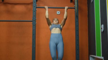 Güzel kaslı sporcu kadın spor salonunun önünde barfiks çekiyor.