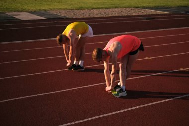 Yarıştan önce stadyumda iki koşucu ısınma egzersizi yapıyor.