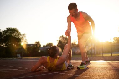 Bir atlet, stadyumda koşarken yaralandıktan sonra ayağa kalkmasına yardım eder.