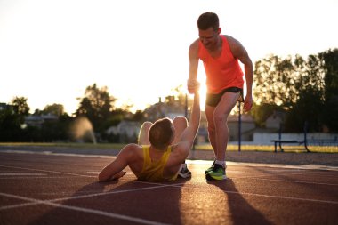 Bir atlet, stadyumda koşarken yaralandıktan sonra ayağa kalkmasına yardım eder.