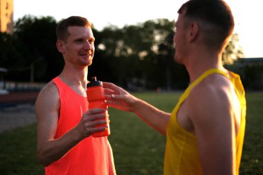 Atletizm sporcuları stadyumda idmandan sonra su içiyorlar.