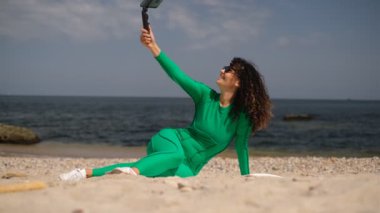 Genç ve güzel bir kadının kumsalda otururken telefonda görüntülü konuşması.