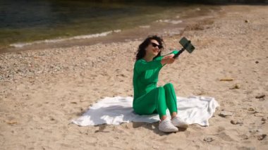 Genç ve güzel bir kadın sahildeki bir video bloğu için telefonda kendini filme alıyor.