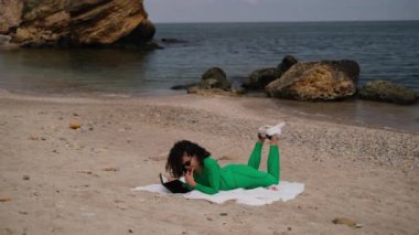 Genç ve güzel bir kadın sahilde kitap okuyor.