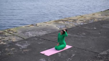 Güzel kadın yoga eğitmeni deniz kıyısındaki bir paspasın üzerinde egzersiz yapıyor.