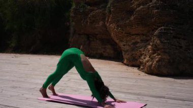Güzel kadın yoga eğitmeni deniz kıyısındaki bir paspasın üzerinde egzersiz yapıyor.