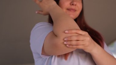 Genç şişman kadın dirseğine masaj yapıyor.