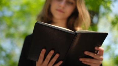 Genç bir kız öğrenci güneşli bir yaz gününde parkta kitap okuyor.