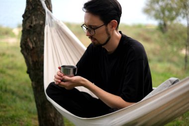 Genç adam deniz kenarındaki bir hamakta dinleniyor.