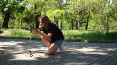 Genç bir kadın blogcunun portresi. Bir yaz günü parkta yayın yapmak için telefonuna kamera koyuyor.