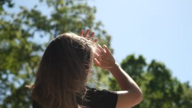 Bir yaz günü parktaki parlak güneşten gözlerini kısarak yüzünü kapatan genç bir kadının portresi.