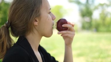 Kırmızı elmayı ısıran genç bir kadının yan görünüm portresi.