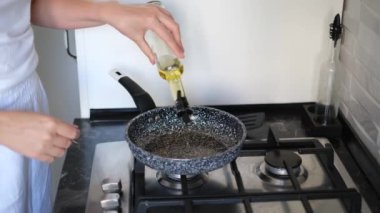 Genç bir kadın kızartma tavasına yağ döker.