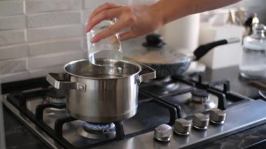 Genç bir kadın gaz ocağında duran tavaya su döker.