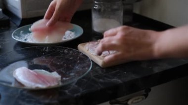Genç kadın kızarmadan önce un içinde tilapia balığı tarıyor.