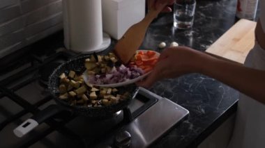 Soğan, patlıcan ve havuçtan tavada sebze sotesi kızartan genç ev hanımı.