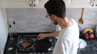 Genç Avrupalı adam mutfağında öğle yemeği için biftek pişiriyor.