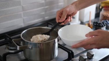 Bir adam sobanın üstünde hindistan cevizi sütü ve bal ile yulaf ezmesi pişirir.