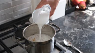 Bir adam sobanın üstünde hindistan cevizi sütü ve bal ile yulaf ezmesi pişirir.