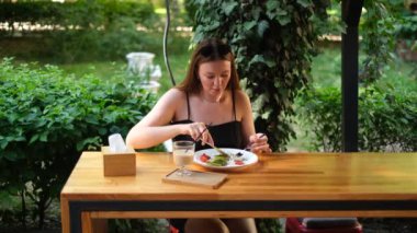 Bir kafede terasta sebze salatası ve kabaklı gözlemelerle kahvaltı eden genç bir kadın.
