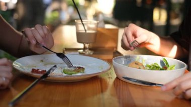 Genç çift salata ve kabaklı gözlemelerle kahvaltı yapıyor. Terasta yakın plan tabaklar bir kafede.