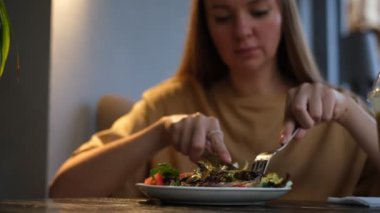 Avrupalı görünümlü genç bir kadın bir kafede sebze salatası yiyor.