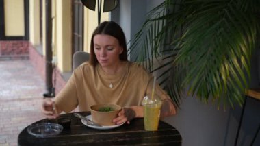 Avrupalı görünümlü genç bir kadın bir kafede sebze salatası yiyor.