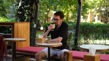 Genç esmer adam sıcak bir yaz gününde terasta kapuçino içer.