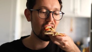 Pizzayı zevkle yiyen esmer bir adamın portresi.