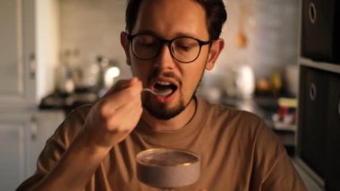 Gözlüklü adam evde meyve suyu içiyor.