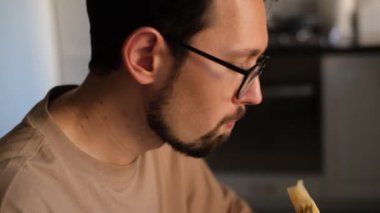 Gözlüklü genç adam evde dilimlenmiş kavun yiyor.