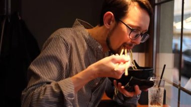 Japon restoranında sakallı ve ramen yiyen genç bir adamın portresi.