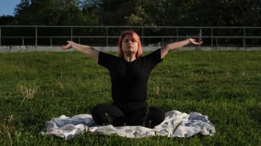 Şişman genç kadın güneşli bir yaz gününde parkta meditasyon yapıyor.