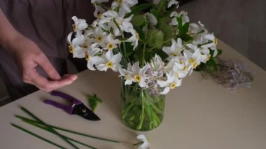 Bir kadın bir buket nergis oluşturur ve onları bir vazo suya koyar.