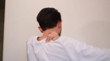 Genç adam omuzlarına ve boynuna masaj yapıyor.