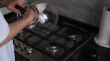 Bir adam mutfakta peçeteyle cam çaydanlığı yıkıyor.