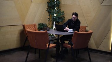 Genç erkek bilişim uzmanı şık bir kafede dizüstü bilgisayar üzerinde çalışıyor.