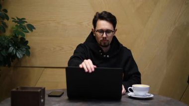 Genç erkek bilişim uzmanı şık bir kafede dizüstü bilgisayar üzerinde çalışıyor.