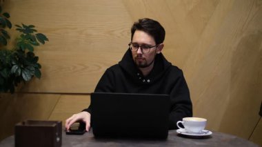 Genç bir adam, bilişim uzmanı, dizüstü bilgisayarın başında otururken telefonla konuşuyor.