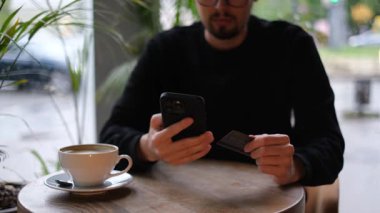 Genç bir adam kredi kartıyla telefonuyla online alışveriş yapıyor.