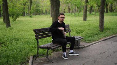 Genç adam parkta bankta otururken termostan fincana çay dolduruyor.