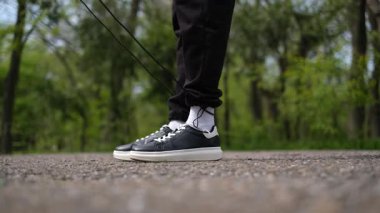 Genç adam spor sahasında ip atlıyor. Parkta bacakları yakın plan.