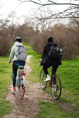 Genç bir çift güneşli bir bahar gününde parkta bisiklet sürüyor.