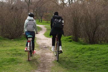 Genç bir çift güneşli bir bahar gününde parkta bisiklet sürüyor.