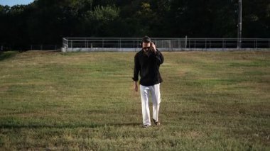 Genç adam gün batımında müzik dinleyerek parkta yürüyor.