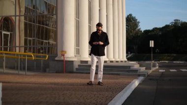 Genç bir adam kulaklıklarını çıkarıp yürürken takıyor. 