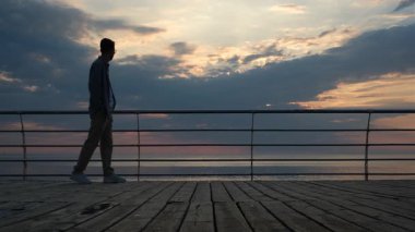 Genç bir adam şafak vakti setin kenarında yürüyor.